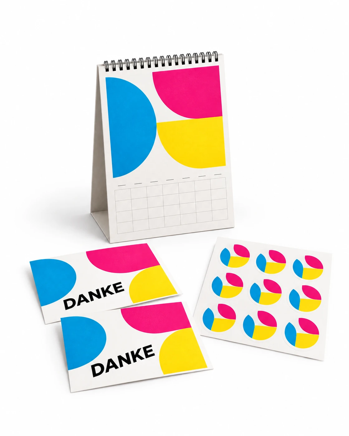 Spiralgebundener Kalender, Postkarten und Aufkleber mit gemeinsamer CMY-Gestaltung auf weißem Hintergrund